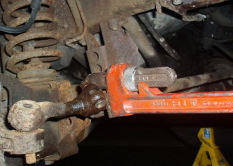 1985 Ford Bronco II - Close-up of a vehicle's tie rod end with a pipe wrench attached, Supermotors.net logo in corner.