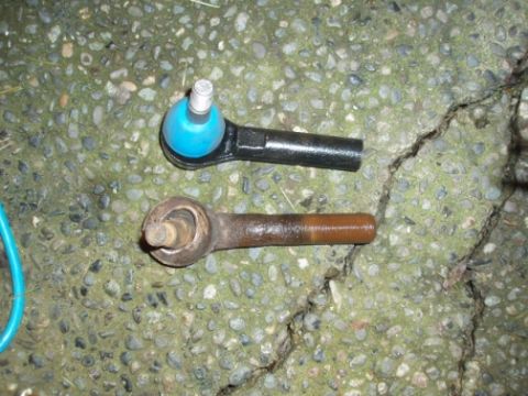 1985 Ford Bronco II - A comparison of a new tie rod end with a heavily rusted old one is shown on a cracked concrete surface.