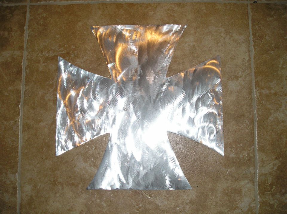 Sheet aluminum Maltese cross with swirled spun finish lying on tile floor