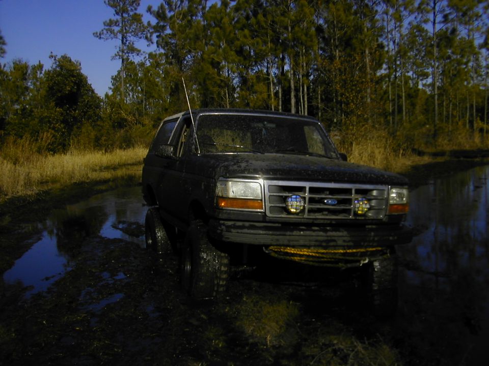 Mud-covered lifted Ford Bronco on large tires standing in a flooded trail
