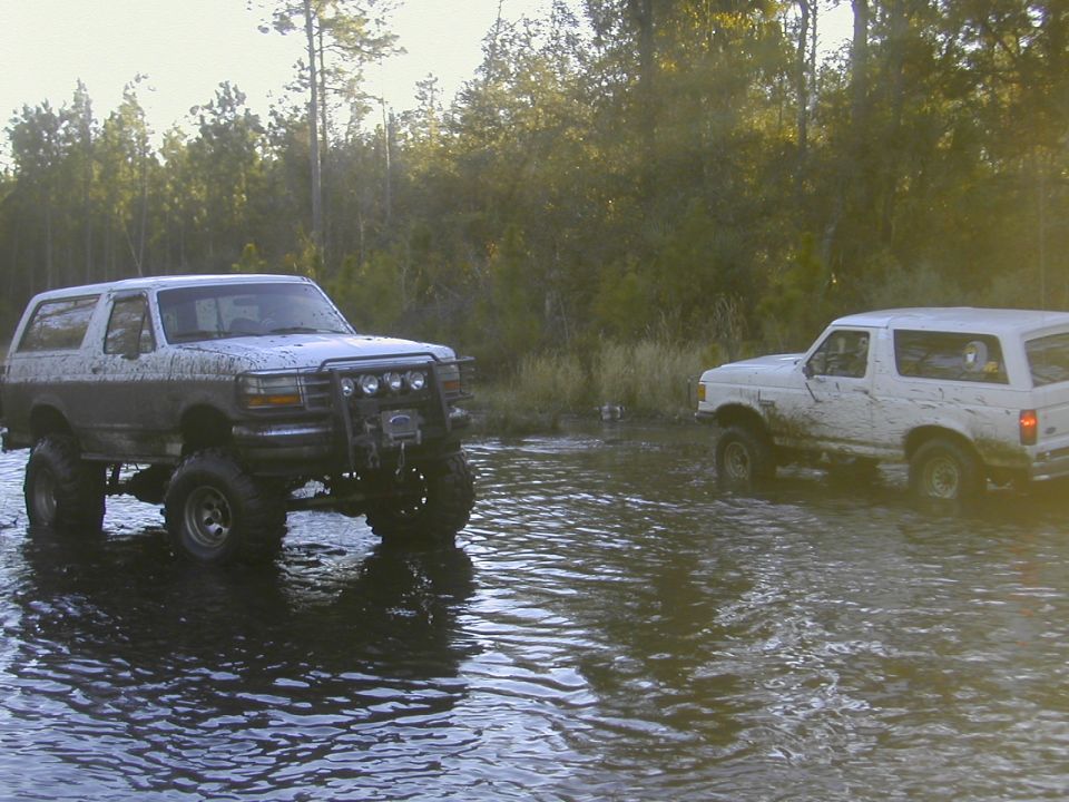 Two lifted Ford Broncos standing in deep water at a flooded trail crossing