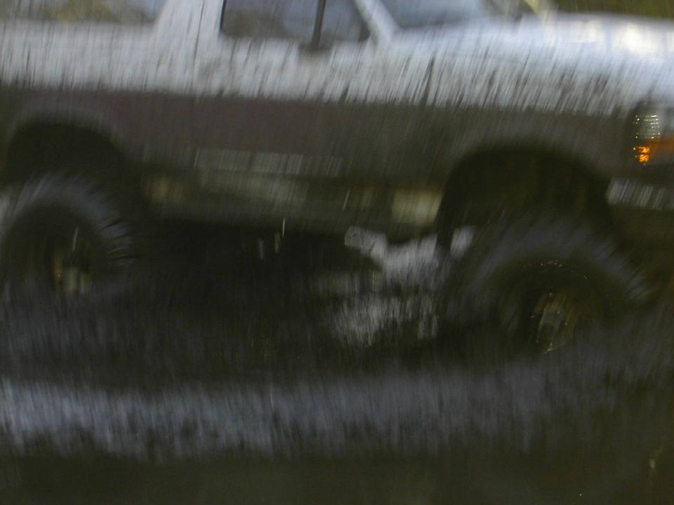 Blurry motion shot of a lifted two-tone pickup truck splashing through water at night