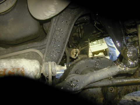 1993 Ford Bronco - Underbody close-up shot from beneath a 4x4, showing a mud-caked front differential housing, radius arm, coil spring and shock mount with a…