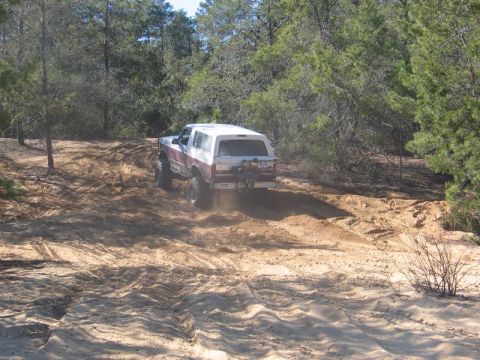 1995 Ford Bronco - A lifted Ford Bronco navigates a sandy trail in a wooded area.