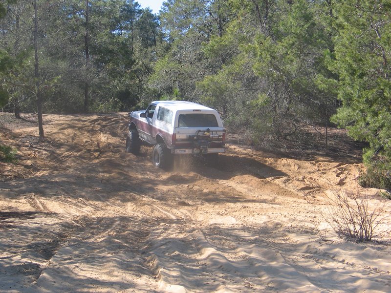 Ford Bronco climbing a sandy hill with trees around