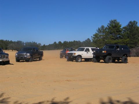 1995 Ford Bronco - A lifted black 1992 Ford Bronco is parked in a sandy area alongside other trucks and SUVs.