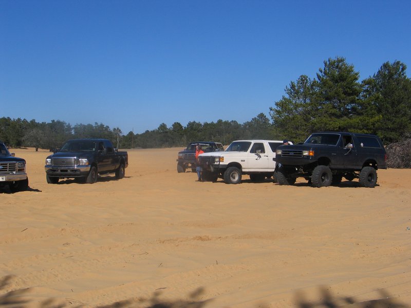 Black lifted 1992 Ford Bronco parked in sand with other vehicles