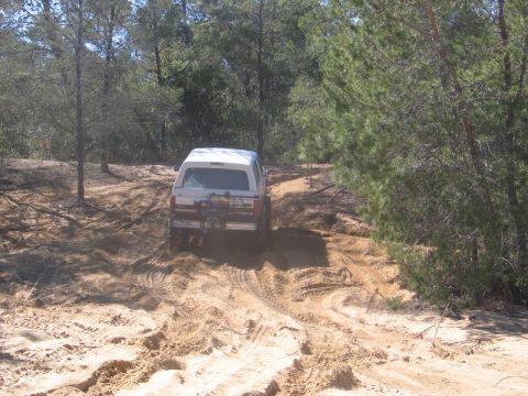 1995 Ford Bronco - White 1995 Ford Bronco navigates a challenging sandy trail in a wooded area.