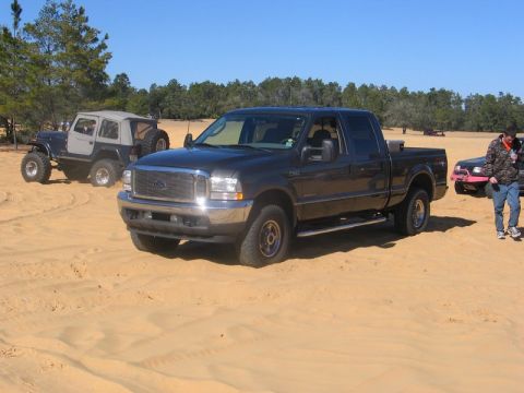 1995 Ford Bronco - Several vehicles are parked on a sandy terrain under a clear blue sky.