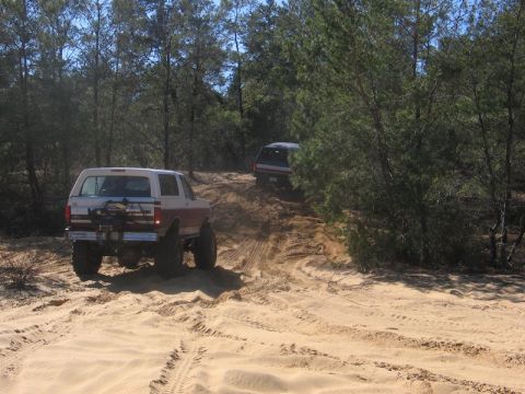 1995 Ford Bronco - Two SUVs navigate a sandy incline in a wooded area.