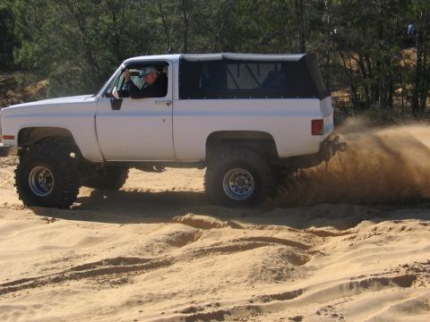 1995 Ford Bronco - A driver navigates sandy terrain in a lifted SUV, sending sand flying.