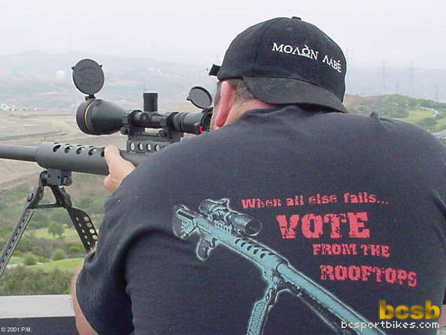 Man aims a scoped rifle mounted on a tripod, wearing a hat with 'MOΛON ΛΑΒΕ' and a t-shirt with a graphic and text