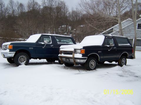 1987 Ford Bronco - Two Ford Broncos are parked in a snowy landscape, one with a protective brush guard on its front end.