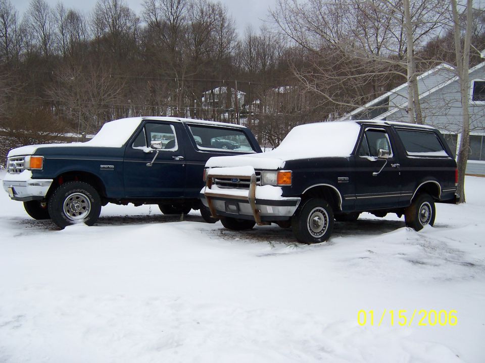 Two dark blue Ford Broncos parked in snow, one with a brush guard