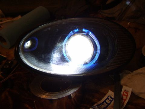 1998 Ford Taurus - Close-up of a custom headlight assembly with a bright white projector and blue halo lighting.