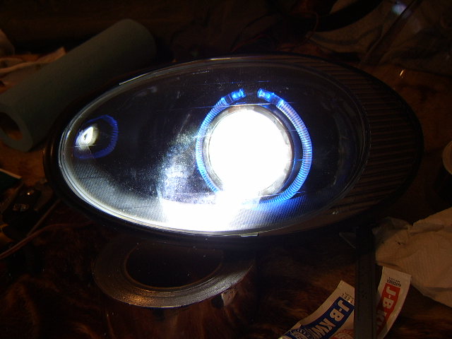 Aftermarket projector headlight with blue LED halo ring, on a table with tools