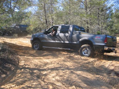 1995 Ford Bronco - A Ford F-250 Super Duty navigates a sandy off-road path, with another vehicle visible in the background.