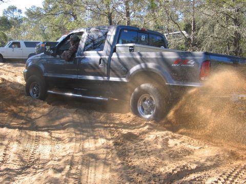 1995 Ford Bronco - A Ford F-Series truck navigates sandy terrain, with another vehicle visible in the background.
