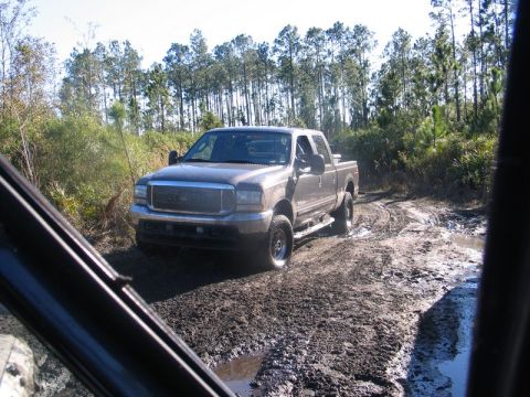 1995 Ford Bronco - A pickup truck navigates a challenging muddy path through a wooded area.