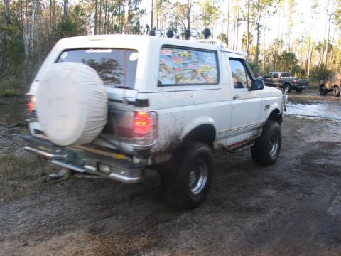 1995 Ford Bronco - A lifted white Ford Bronco is seen off-road with other vehicles in the background.