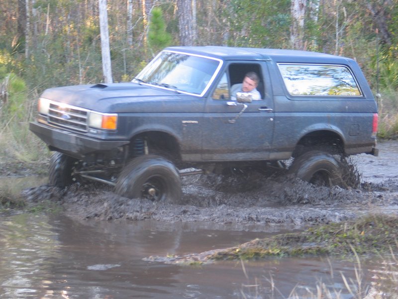 Dark blue lifted 1995 Ford Bronco driving through mud