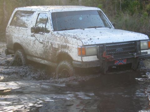 1995 Ford Bronco - This Ford Bronco is deep in the mud, navigating a water obstacle with a Confederate flag displayed.