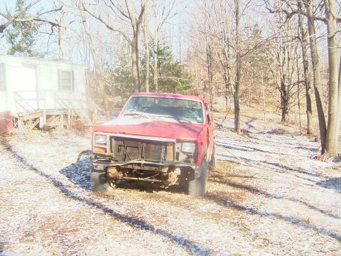 1984 Ford Bronco - A red pickup truck sits in a yard with snow on the ground and trees in the background.