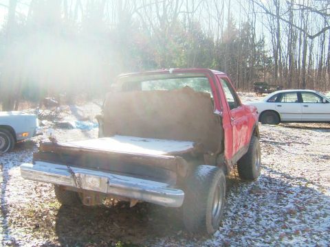1984 Ford Bronco - Red pickup truck with a wooden bed modification, parked outdoors with snow on the ground. A white sedan is visible in the background.
