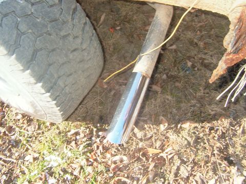 1984 Ford Bronco - Close-up of a vehicle's exhaust pipe and tire, with debris on the ground.