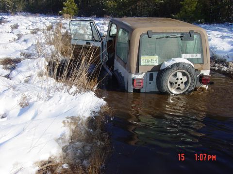 1995 Dodge 1500 - A Jeep Wrangler is partially submerged in murky water, with snow and reeds on the shore.