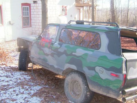 1984 Ford Bronco - Camouflaged SUV with a roof rack is parked outside a building.
