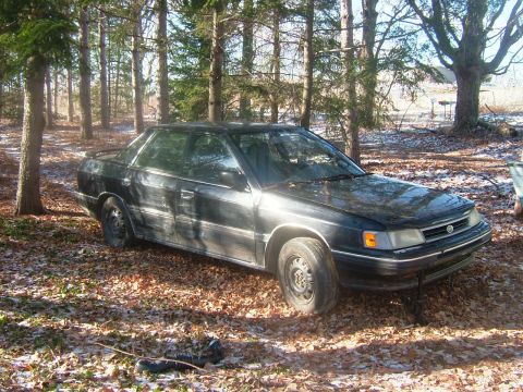 1984 Ford Bronco - This black sedan, likely a 1989 model, sits parked amongst trees in a natural setting.