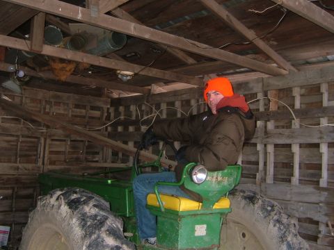 1984 Ford Bronco - A man wearing an orange hat sits in the driver's seat of a green tractor inside a wooden structure.