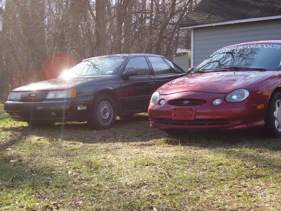 Red 1997 Ford Taurus front 3/4 view next to a dark sedan