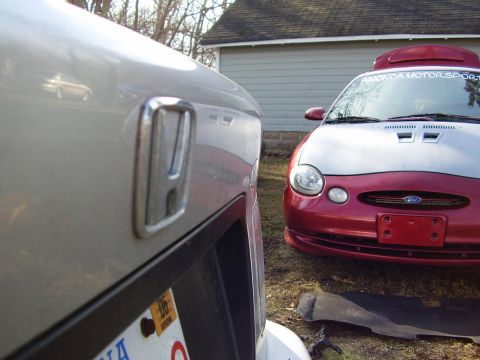 1997 Ford Taurus - Honda emblem is in foreground, with a red Ford Taurus visible behind it.