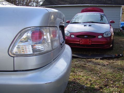 1997 Ford Taurus - A red and silver car with a hood scoop and a sticker on the windshield is parked outside.