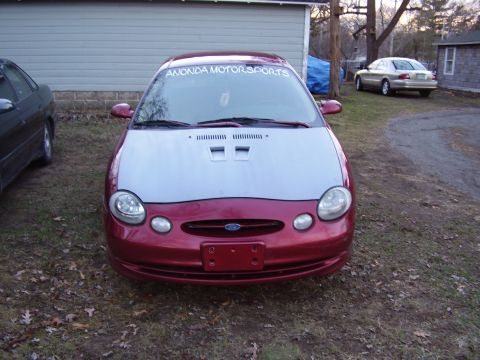 1997 Ford Taurus - A red Ford Taurus with a silver hood is parked in a yard with another car visible.