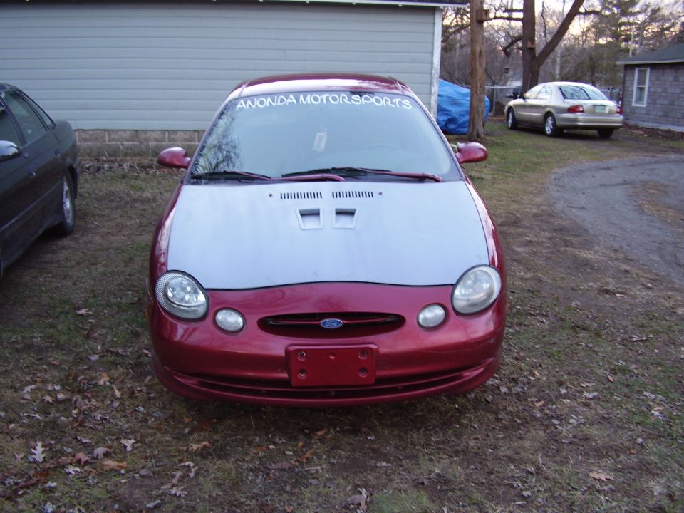 Red Ford Taurus with a silver hood, parked outdoors
