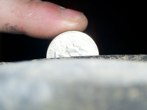 1977 Ford F-150 - A close-up shot shows a finger holding a quarter coin above a rough, textured surface.