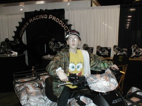 1979 Ford Bronco - A person poses on an ATV in front of a booth displaying various products and a large gear logo.