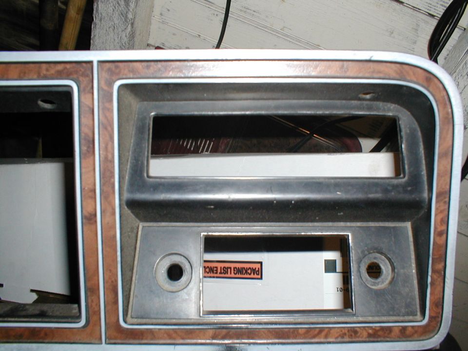 Dashboard trim with wood grain accents, openings for a radio and gauges. A "PACKING LIST ENCL" sticker is visible