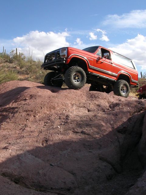 1984 Ford Bronco - This red SUV is navigating a steep, rocky incline in a desert landscape.