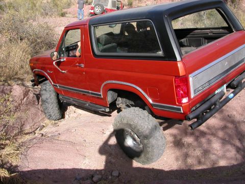 1984 Ford Bronco - A red Ford Bronco navigates a rocky trail, with another vehicle visible in the background.