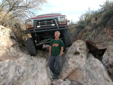 1984 Ford Bronco - A man poses in front of a lifted red 1984 Ford Bronco navigating a rocky trail.