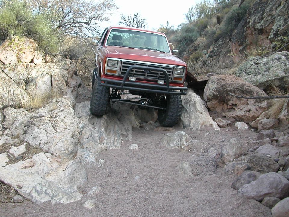 Red Ford Bronco navigating a rocky trail with aftermarket bumper and large tires