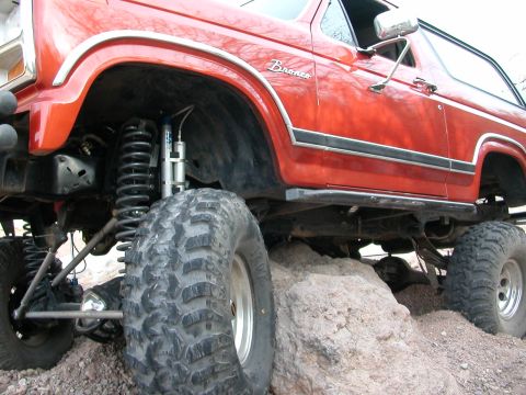 1984 Ford Bronco - This lifted 1984 Ford Bronco is shown navigating a rocky terrain, highlighting its off-road capabilities.