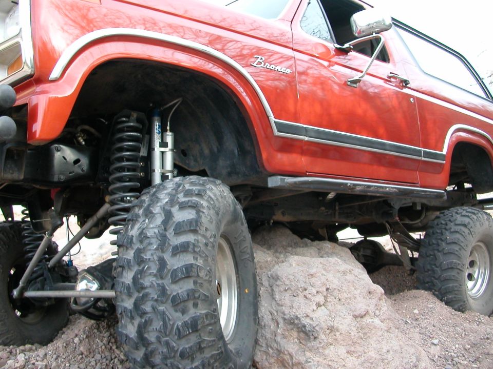 Red lifted Ford Bronco with large tires on rocks. Shows suspension and side profile