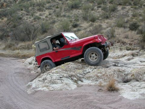 1984 Ford Bronco - A red Jeep Wrangler navigates a rocky off-road trail.