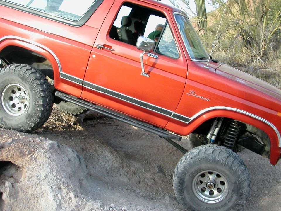 Orange 1984 Ford Bronco with large tires on rocky terrain