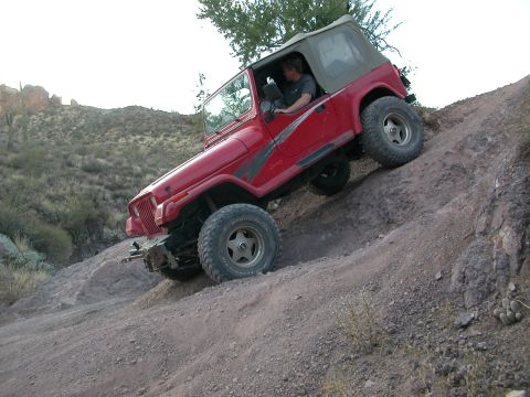 1984 Ford Bronco - Jeep Wrangler navigates challenging off-road terrain on a steep incline.